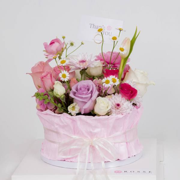 Pastel pink and lavender mixed flowers in a round pink hatbox with a thank you card.