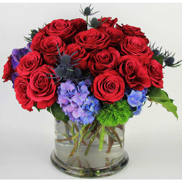 Red roses and blue hydrangeas in a clear glass vase