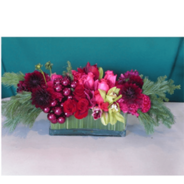 Rectangular floral arrangement with pink, red, and purple blooms in a green container