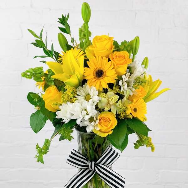 Yellow and white mixed bouquet in a glass vase with a striped ribbon
