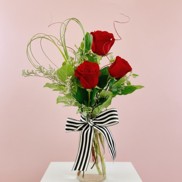 Three red roses in a glass vase with a black-and-white striped bow