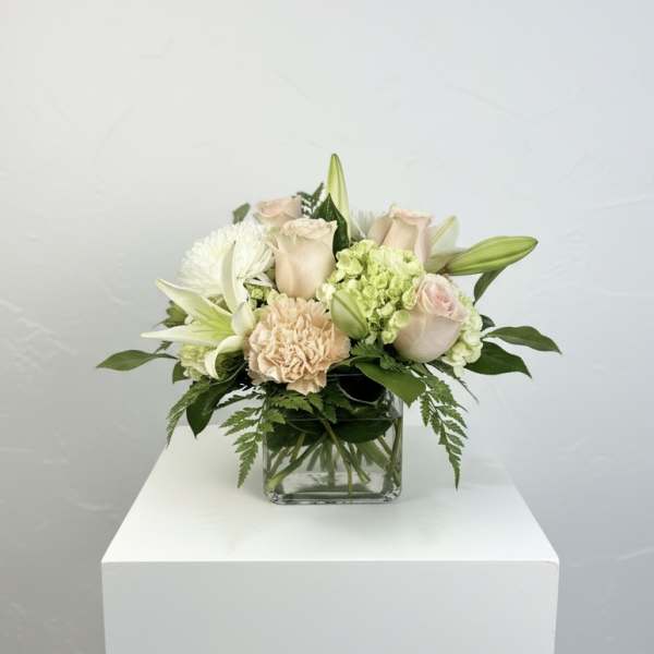 Cream roses and white lilies arranged in a clear glass vase