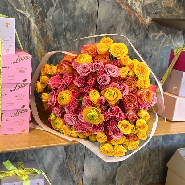 Large bouquet of pink and yellow roses wrapped in pale paper