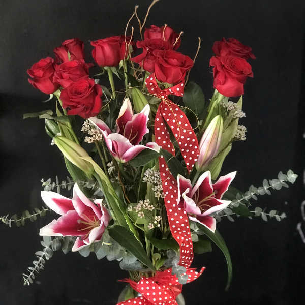 Bouquet of red roses and pink lilies with a polka-dot ribbon in a glass vase