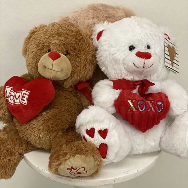 Two plush teddy bears holding red heart pillows on a white stool