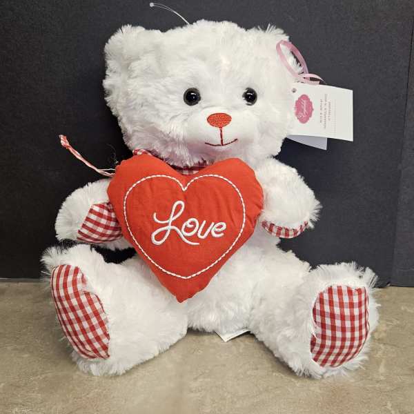 White teddy bear holding a red heart pillow with the word Love