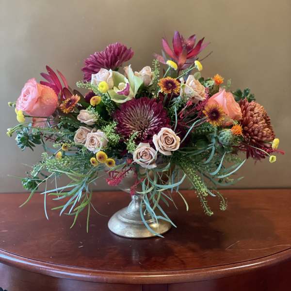 Mixed pink and burgundy flowers arranged in a silver pedestal vase