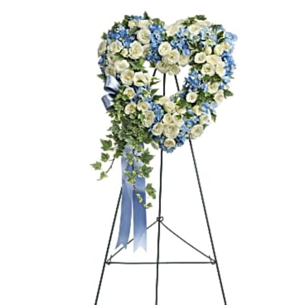 Heart-shaped blue and white sympathy wreath on a metal easel with trailing ivy and blue ribbon.