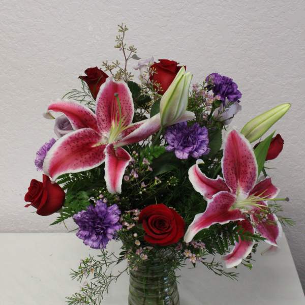Bouquet of pink lilies, red roses, and purple flowers in a glass vase