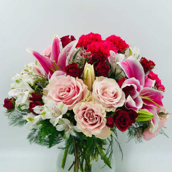 Mixed bouquet of pink lilies, roses, and carnations in a glass vase