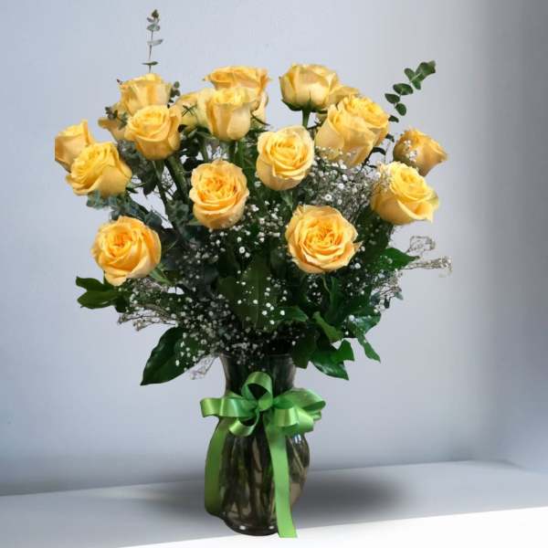 Arrangement of yellow roses with white filler flowers in a clear vase tied with a green ribbon
