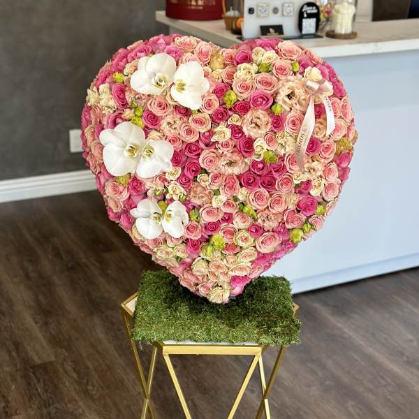 Heart-shaped floral arrangement of pink roses with white orchids on a stand