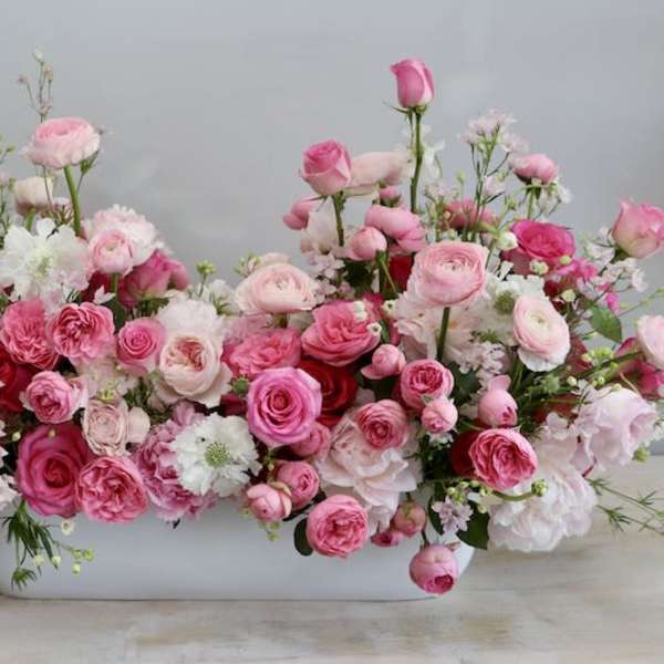 Low centerpiece of pink and white roses and ranunculus in a long white container