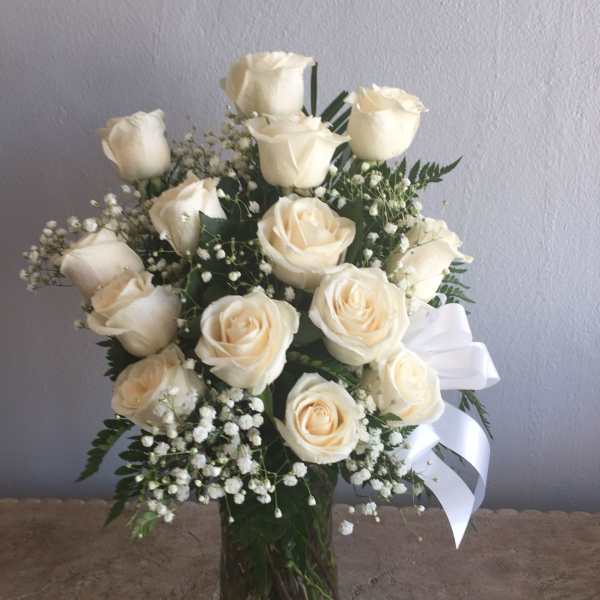 Cream rose bouquet in a clear glass vase with baby's breath and a white ribbon
