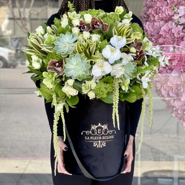 Large bouquet of white orchids, succulents, and green blooms in a black box