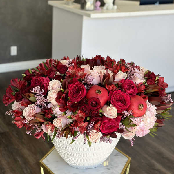 Large red and pink floral arrangement in a white vase with pomegranates