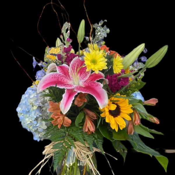 Mixed bouquet with pink lily, sunflowers, and blue hydrangea in a glass vase