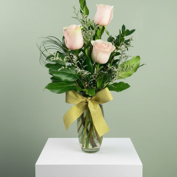 Three pale pink roses in a glass vase with a gold ribbon