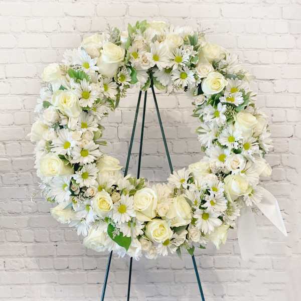 White floral wreath on a stand with roses and daisies