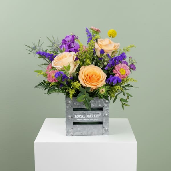 Mixed bouquet of peach roses and purple flowers in a metal crate