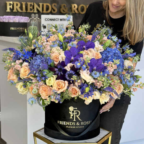 Large mixed bouquet in a black hat box with peach, blue, and purple flowers
