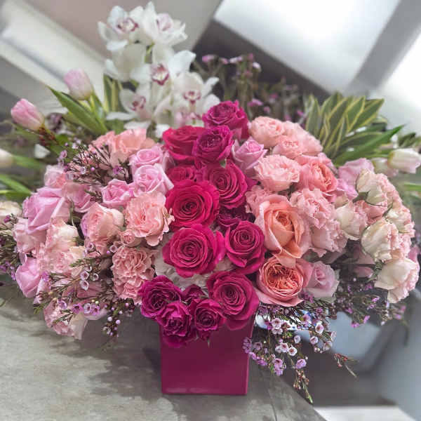 Pink and white rose arrangement in a magenta vase with orchids