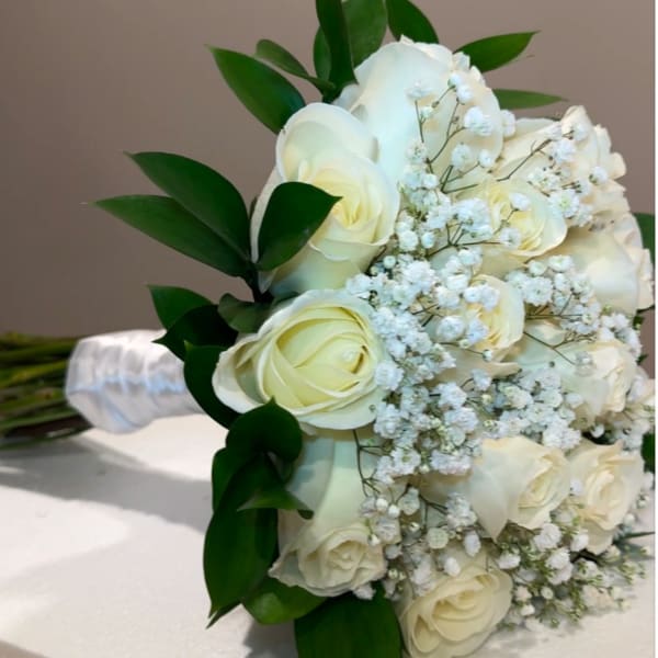 White rose bridal bouquet with baby's breath and dark green leaves