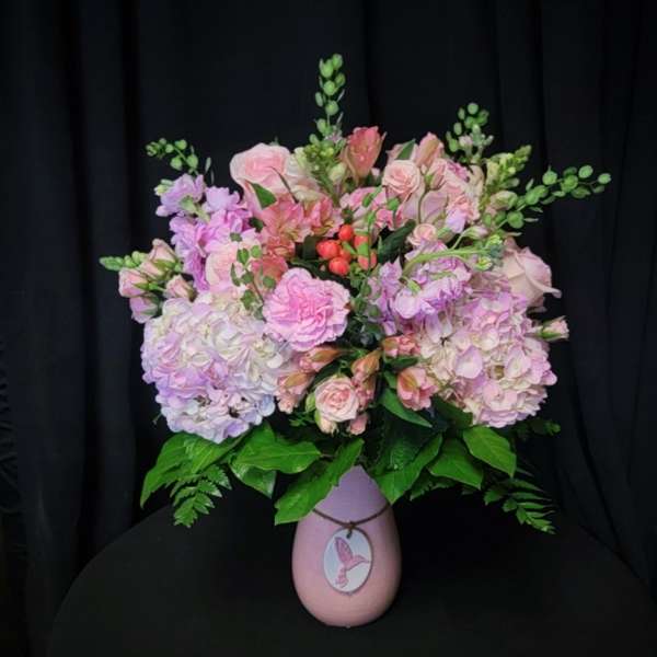 Pink and lavender floral arrangement in a pink vase with a bird tag
