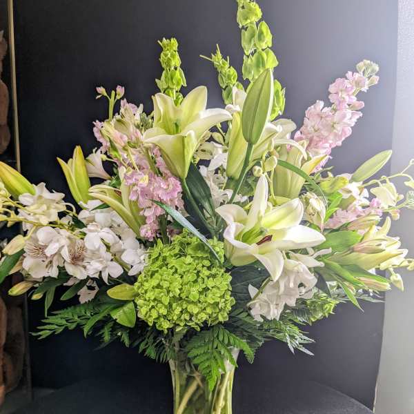 Tall bouquet of white lilies, pink blooms, and green hydrangea in a glass vase