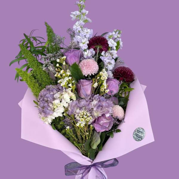 Lavender bouquet with roses, hydrangeas, and mixed blooms wrapped in pink paper