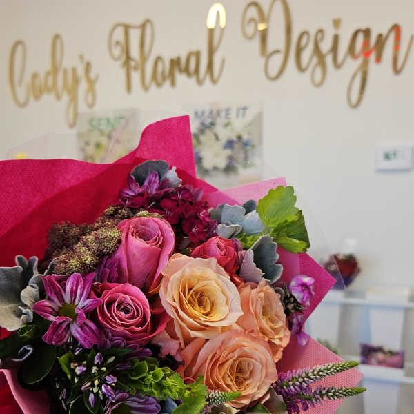 Handheld bouquet of pink, peach, and purple roses with mixed blooms