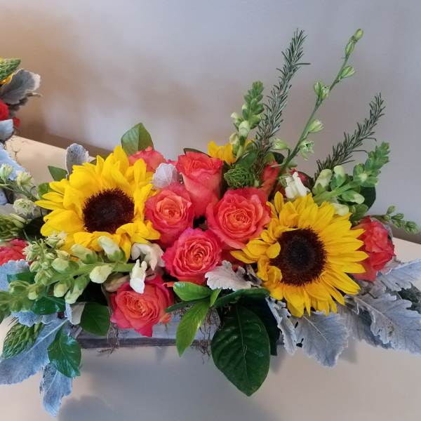 Bright bouquet with sunflowers and coral roses in a low rectangular container