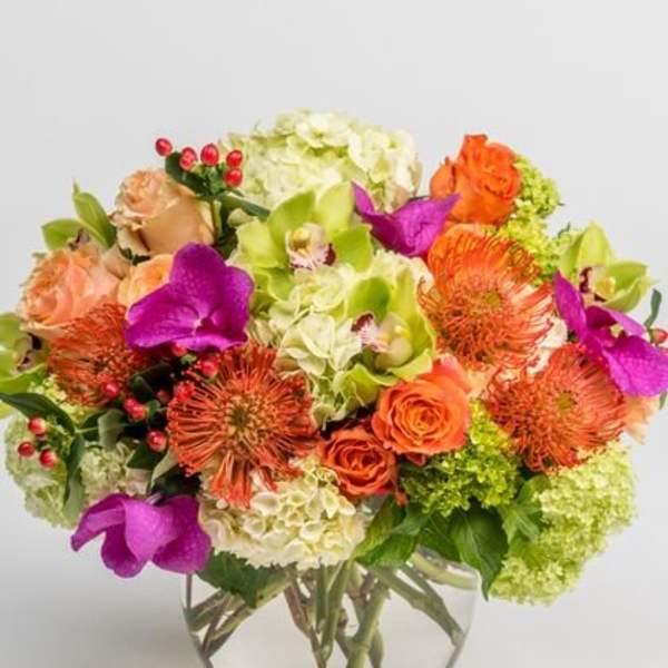 Mixed bouquet of orange, purple, and green flowers in a clear glass vase