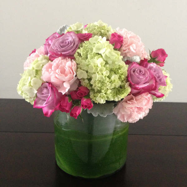 Pink and lavender flowers arranged in a green glass vase