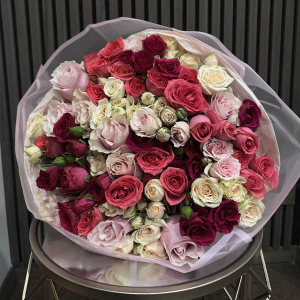 Large bouquet of pink, red, and cream roses wrapped in pale paper