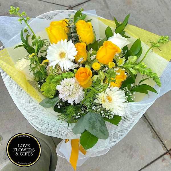 Hand-tied bouquet of yellow roses and white gerbera daisies wrapped in white and yellow mesh.
