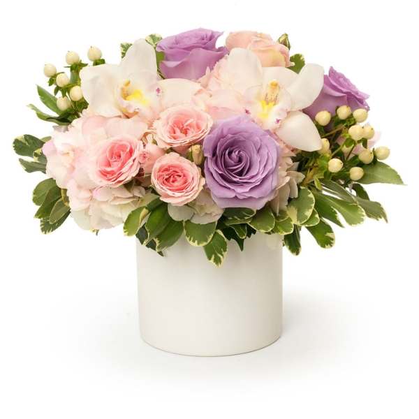 Pastel roses and white orchids arranged in a white vase