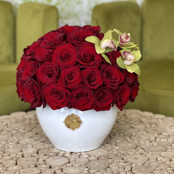 Red rose arrangement in a white vase with small orchid accents