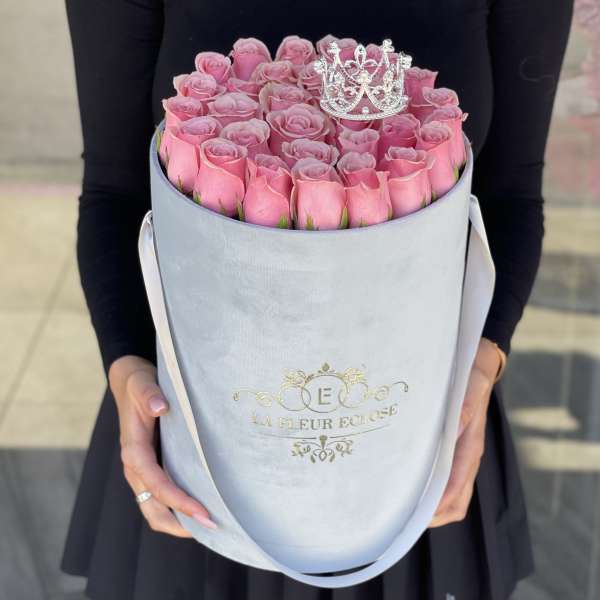 Pink roses arranged in a round hatbox with a small crown topper