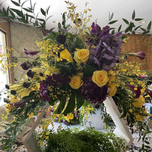 Large floral arrangement with yellow roses and purple orchids in a geometric stand