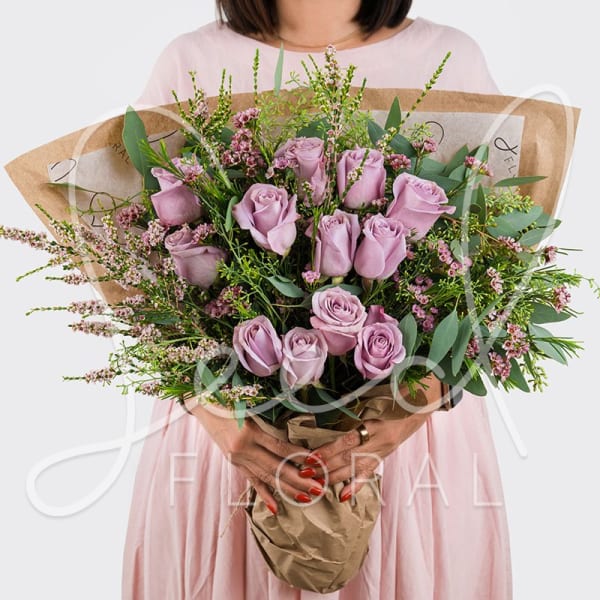 Hand-tied bouquet of lavender roses with pink filler flowers wrapped in brown kraft paper