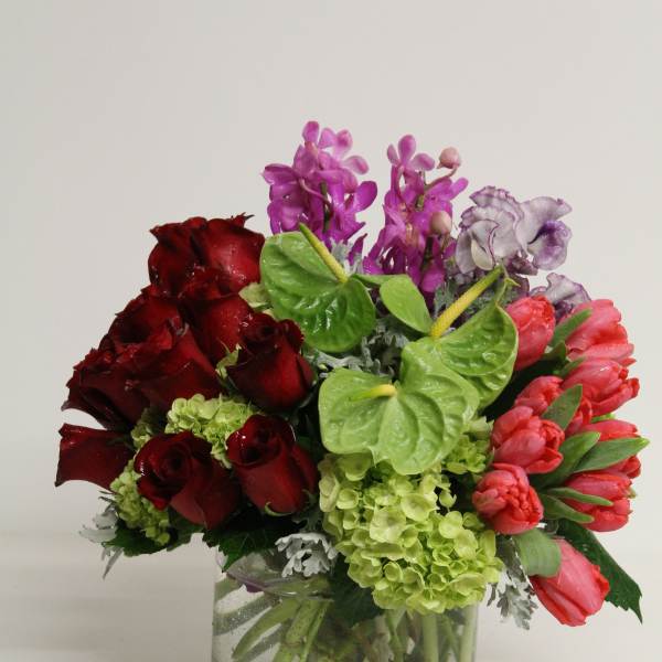 Mixed arrangement of red roses, pink tulips, and purple blooms in a clear glass vase