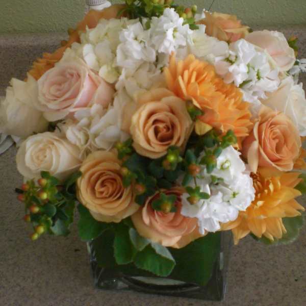 Peach and white roses with orange blooms in a glass vase