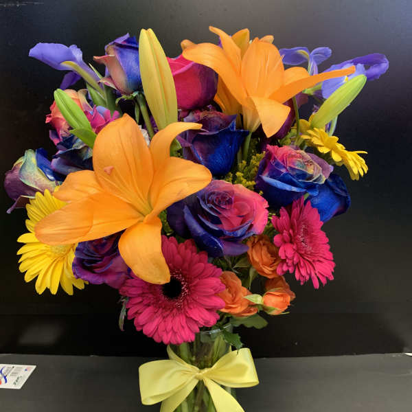Bright mixed bouquet with orange lilies, dyed roses, and pink daisies in a glass vase