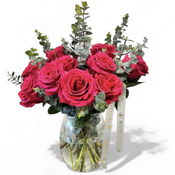 Hot pink roses arranged in a clear glass vase with eucalyptus