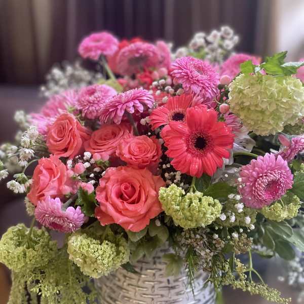 Pink and coral mixed bouquet in a white basket vase