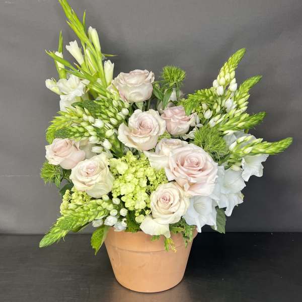 Blush roses and white flowers arranged in a peach pot