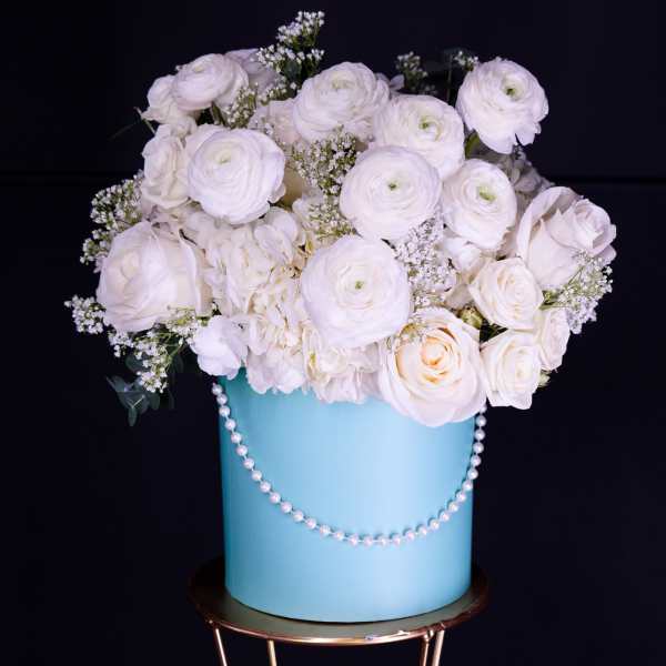 White roses and ranunculus in a blue hatbox with a pearl garland