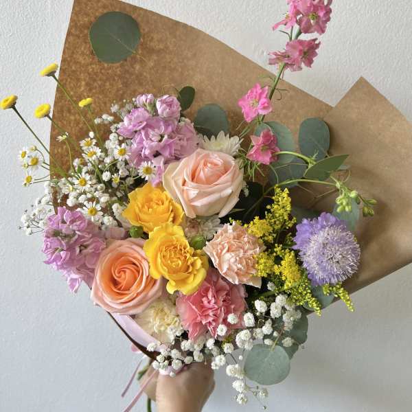 Hand-tied bouquet of pink, peach, and yellow flowers wrapped in brown paper