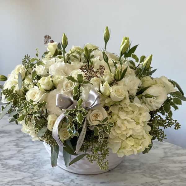 White rose and hydrangea arrangement in a white bowl with a silver ribbon